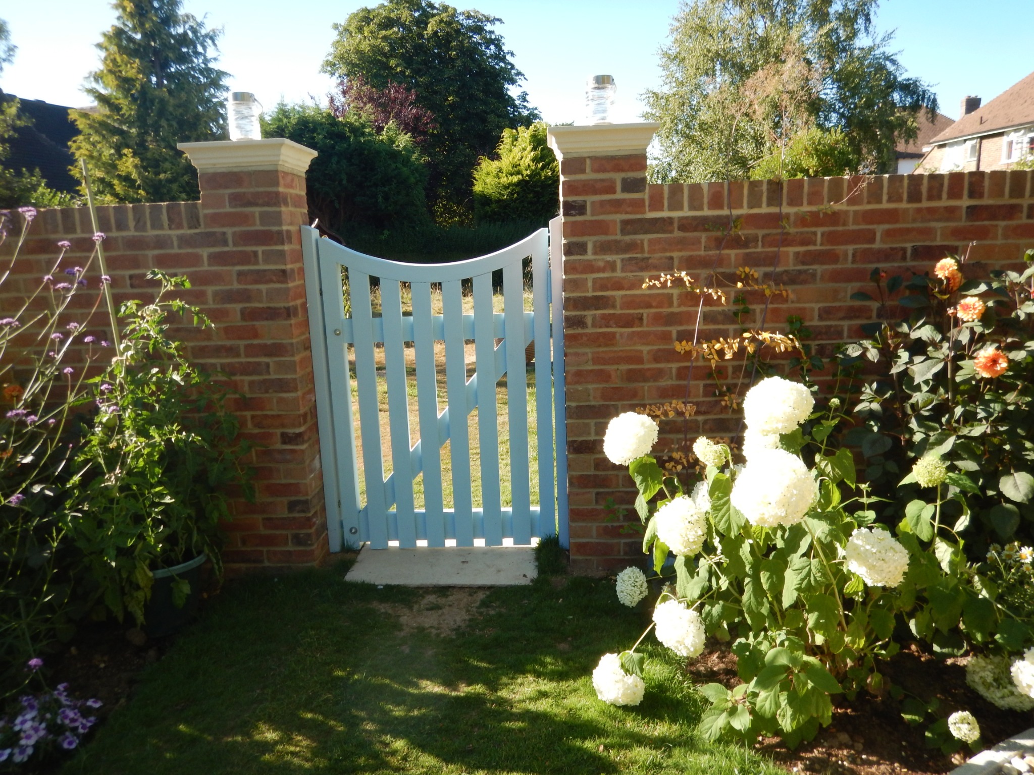 Pale blue timber garden gate with a curved top between brick pillars